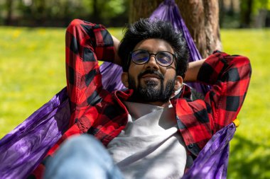 Hindu genç adam hamakta yatarken parkta günün tadını çıkarıyor.