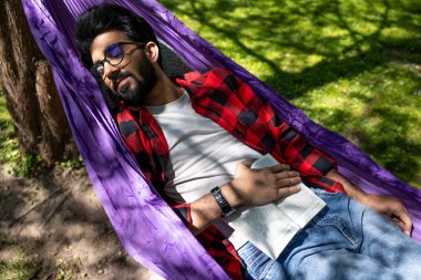 Esmer genç adam parkta hamakta uyuyor.