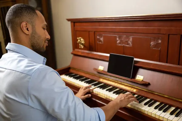 Cheerful man practicing playing piano in living room of his home relaxing from work