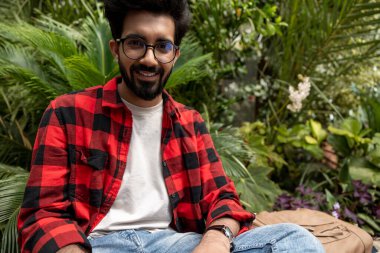 Kırmızı kareli gömlekli bir adam bahçede dizüstü bilgisayarla çalışıyor.