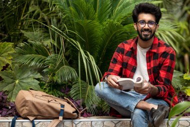 Hindu genç adam elinde kitapla bahçede oturuyor.