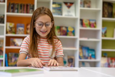 Gülümseyen kahverengi saçlı okul kütüphanesinde ders için hazırlanıyor..