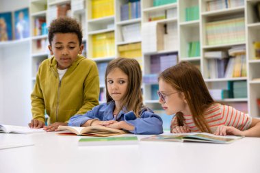 Çok ırklı bir grup çocuk ilkokul kütüphanesinde okuyor..