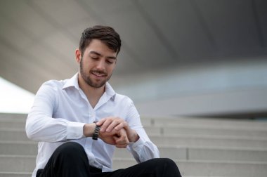 Kendine güvenen bir adam. Beyaz gömlekli kendine güvenen genç adam merdivenlerde oturuyor.