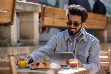 Bir kafede. Koyu saçlı Hintli adam pizza yiyor ve dizüstü bilgisayarla çalışıyor.