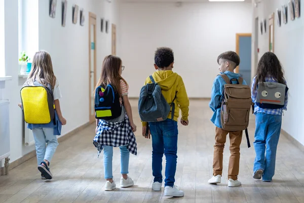 Back view of group of elementary school kids standing in school corridor during break.
