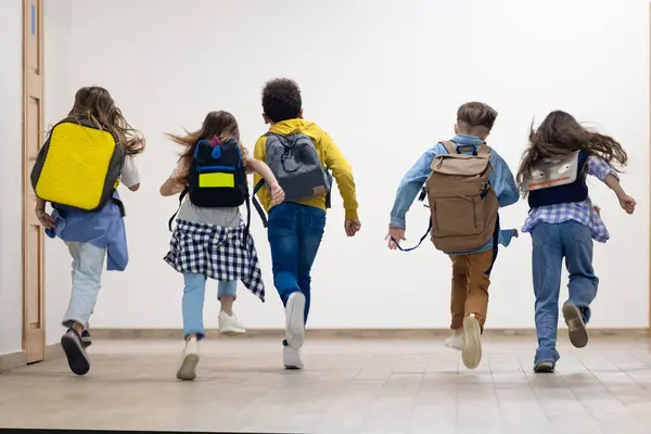 Group of elementary school kids running in school corridor during break.