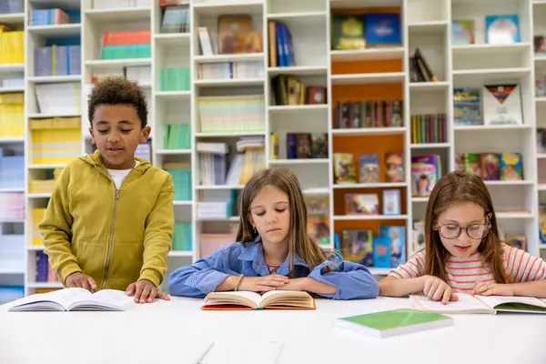 Çok ırklı bir grup çocuk ilkokul kütüphanesinde okuyor..