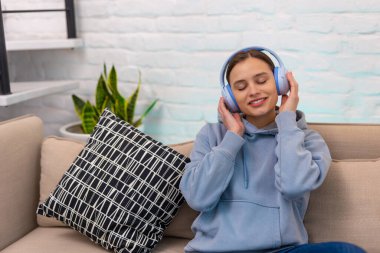 Oturma odasındaki kanepede oturmuş müzik dinleyen neşeli genç kız..