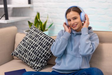 Oturma odasındaki kanepede oturmuş müzik dinleyen neşeli genç kız..