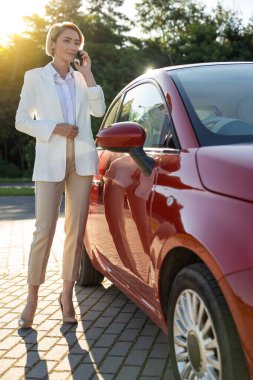 Başarılı bir iş kadını, arabasının yanında cep telefonuyla konuşma yapıyor.