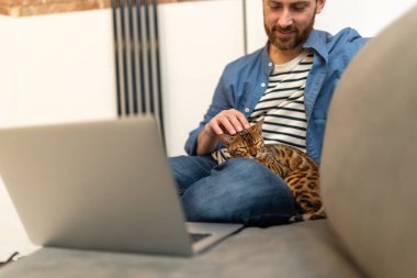 Kot ceketli ve pantolonlu bir adam evde dizüstü bilgisayarla çalışıyor.