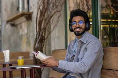 Boş zaman. Elinde kitapla, koyu saçlı, kulaklıklı, Hintli genç bir adam.