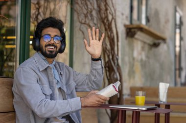 Boş zaman. Elinde kitapla, koyu saçlı, kulaklıklı, Hintli genç bir adam.