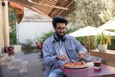 Pizzacı. Kafede masada oturan bir adam pizza kesiyor.