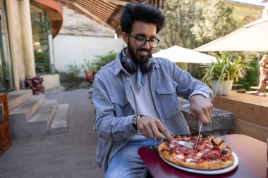 Pizzacı. Kafede masada oturan bir adam pizza kesiyor.