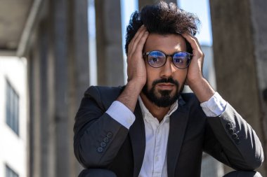 Genç Hintli işadamı merdivenlerde oturuyor ve yorgun ve stresli görünüyor.