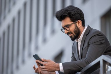 Gülümseyen yakışıklı Hindu adam telefonda mesaj atıyor ve mutlu hissediyor.