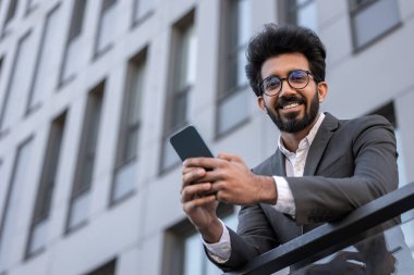 Gülümseyen yakışıklı Hindu adam telefonda mesaj atıyor ve mutlu hissediyor.