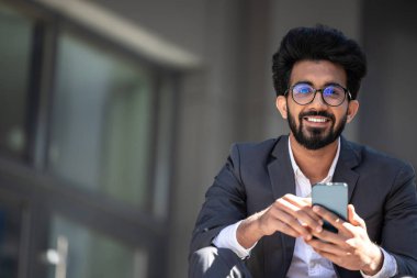 Koyu renk saçlı Hintli adam merdivenlerde elinde telefonla oturuyor.