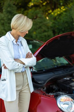 Yolda bozuk otomobilin yanında duran sarışın kadının motor sorunu var.