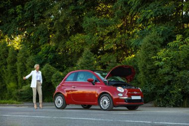 Bir kadının parmağını kaldırması, sürücülerin kaputu kırık bir şekilde arabanın yanında durmasını engelliyor.