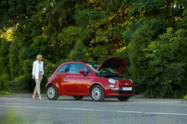 Kaputu patlamış, bozuk bir arabanın yanında duran genç bir kadın aracıyla sorun yaşıyor.