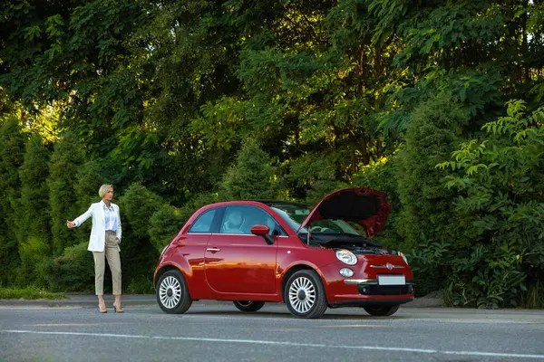 Bir kadının parmağını kaldırması, sürücülerin kaputu kırık bir şekilde arabanın yanında durmasını engelliyor.