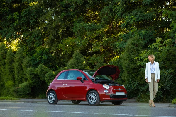 Yolda bozuk otomobilin yanında duran sarışın kadının motor sorunu var.