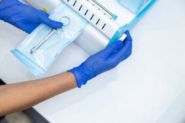 Tanımlanamayan dişçi mavi eldivenli elleri dişçi aletlerini sterilize kutusunu kullanarak tutuyor.