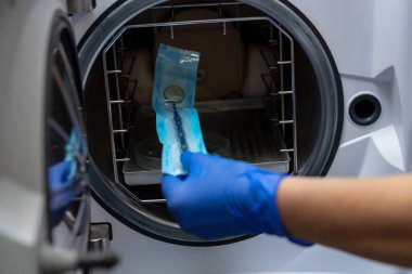 Bilinmeyen diş hekimi elinde mavi eldivenlerle dişçi aletlerini sterilize ediyor.