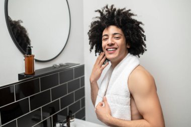 Sabah prosedürleri. Esmer, kıvırcık saçlı adam banyoda sabah prosedürü uyguluyor.