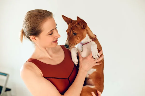 Beautiful sporty woman holding dog in fitness studio