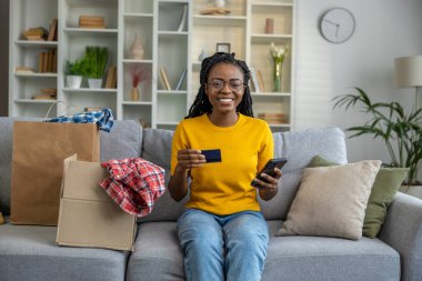 Elinde kredi kartıyla gülümseyen esmer tenli bir kadın.