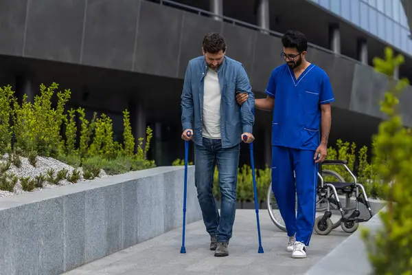 Walking together. Man with sticks walking with a male nurse