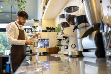 Kahvesini kafede demleyen adam profesyonel yeteneklerini sergileyen fincanlara buharlı espresso dolduruyor.