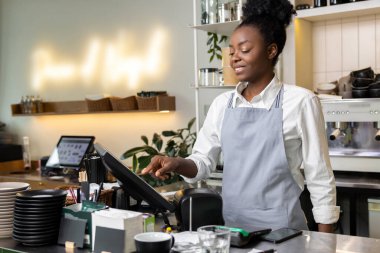 Terminal bilgisayar kullanarak kafe tezgahında duran çok kültürlü kadın garson.