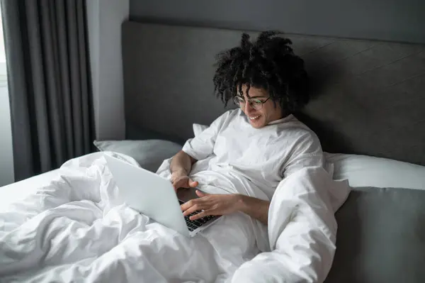 Uzaktan Kumanda Beyaz Tişörtlü Esmer Adam Yatakta Yatıyor Dizüstü Bilgisayarla — Stok fotoğraf