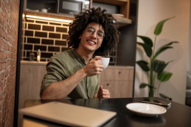 Kahve molası. Kıvırcık saçlı genç adam masada oturuyor ve kahve içiyor.