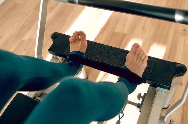 Kapalı spor salonunda pilates simülatöründe bacak egzersizi yapan tanınmayan bir kadın.