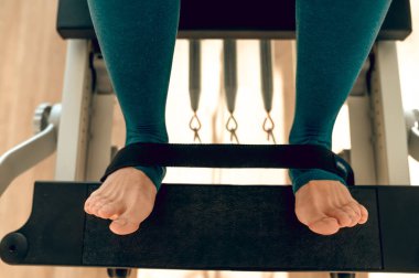 Kapalı spor salonunda pilates simülatöründe bacak çalıştıran tanınmayan bir kadın.