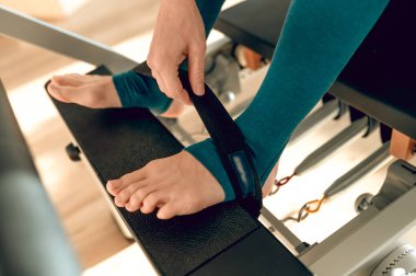 Kapalı spor salonunda pilates simülatöründe bacak egzersizi yapan tanınmayan bir kadın.