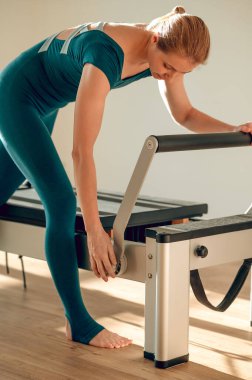 Güzel sarışın kadın spor stüdyosunda pilates makinesi kuruyor.