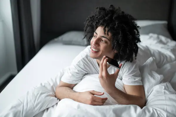 Pesan Suara Pria Berambut Keriting Berbaring Tempat Tidur Dan Mendengarkan — Stok Foto