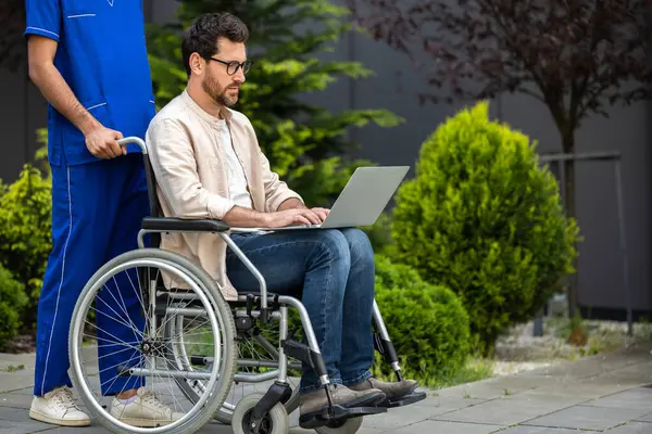 Connected. Young man in wheelchair with laptop in a hospital yard
