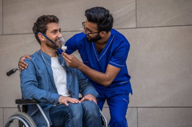 Dikkat et. Erkek hemşire tekerlekli sandalyedeki hastaya oksijen maskesi takıyor.