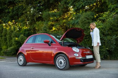 Sarışın kadın sürücü akıllı telefon kullanıyor. Yolda dururken bozuk arabasıyla sorun yaşıyor.