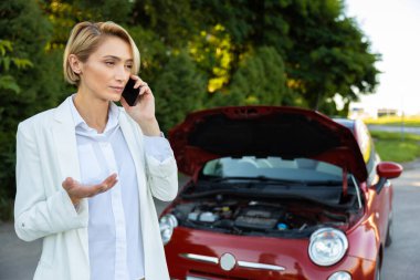 Sarışın kadın sürücü akıllı telefon kullanıyor. Yolda dururken bozuk arabasıyla sorun yaşıyor.