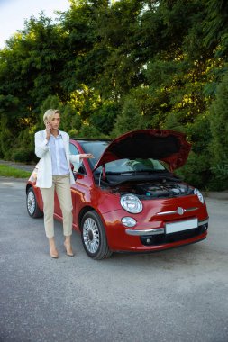 Sarışın kadın sürücü akıllı telefon kullanıyor. Yolda dururken bozuk arabasıyla sorun yaşıyor.