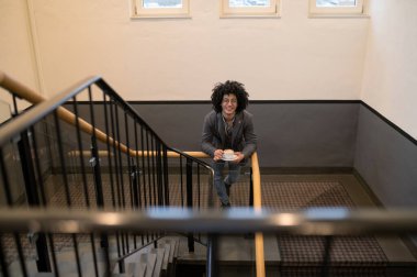 Kahve içiyorum. Merdivenlerde elinde bardakla gözlüklü, kıvırcık saçlı genç adam.